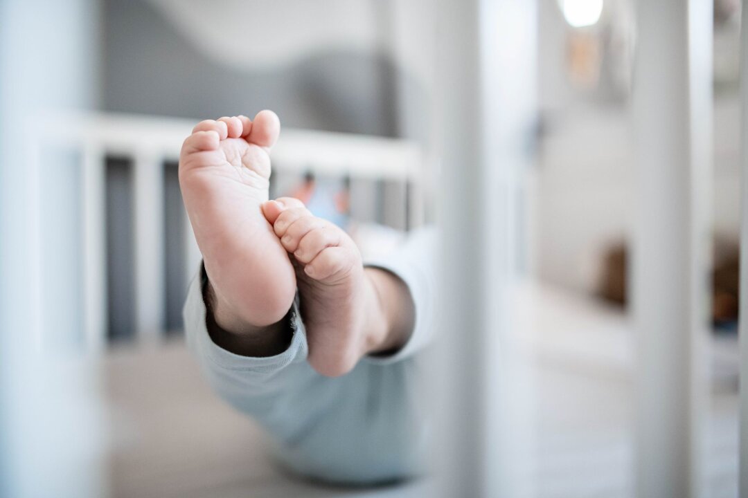 Das waren 2023 die beliebtesten Babynamen in Sachsen - Die Füße eines Babys sind in einem Kinderbett zu sehen.