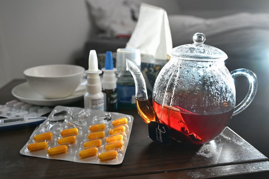 Immer weniger Atemwegsinfektionen: Grippewelle vorbei - Medikamente und eine Kanne und Tasse Tee sind auf einem Nachttisch aufgestellt.