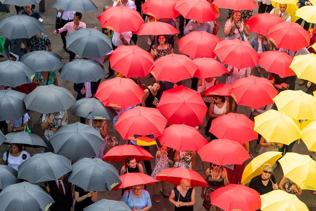 2023 erneut mehr Einbürgerungen von Ausländern in Sachsen - Eingebürgerte Menschen stehen mit schwarz-rot-goldenen Regenschirmen nach dem Einbürgerungsfest vor dem Sächsischen Landtag.