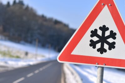 7 Tipps, wie Sie mit dem Auto sicher durch den Winter kommen - Dieses Warnschild weist auf einer Straße auf Straßenglätte hin.