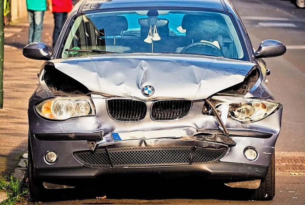 Alkoholisierter Autofahrer gefährdet schwangere Frau - Symbolbild. Ein Wagen der Merke BMW mit erheblichen Unfallschäden. In der Windschutzscheibe baumeln Baby-Schuhe. Foto: Pixabay