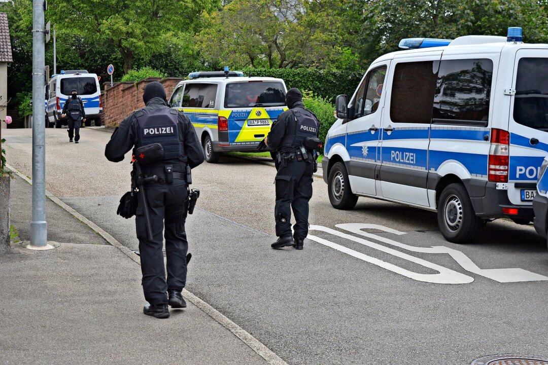 Bei "Reichsbürger"-Razzia Bagger und Gabelstapler im Einsatz - Polizeifahrzeuge und -beamte stehen auf einer Straße.