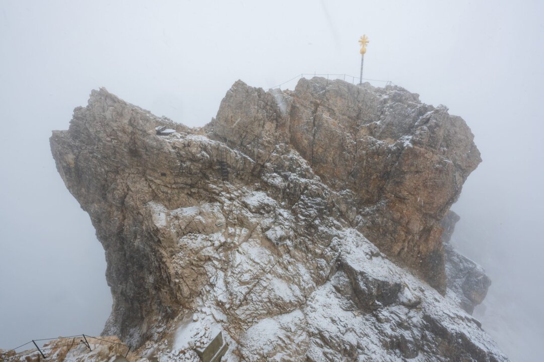 Bergnot: Bergsteiger im Schneetreiben an Zugspitze gerettet - Nebelwolken umhüllen bei Schneetreiben auf der Zugspitze die Aussichtsplattform mit dem Gipfelkreuz (Archivbild). Aus 
mehreren Bergsteigergruppen wurden Notrufe abgesetzt, nachdem sie aufgrund von Witterung und Neuschnee auf etwa 2500 Metern Höhe nicht mehr weiterkamen.