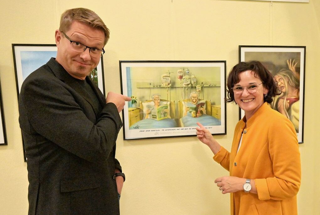 Der Karikaturist Veit Schenderlein (li.) zeigt eine Auswahl seiner Arbeiten im Kirchberger Rathaus, was Bürgermeisterin Dorothee Obst (re.) freut. Foto: Ralf Wendland