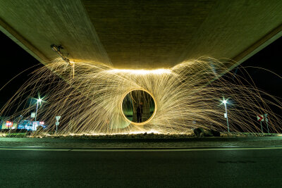 Unter einer Brücke fliegen die Funken der Lichtkunst in kreisform weg von der Mitte.