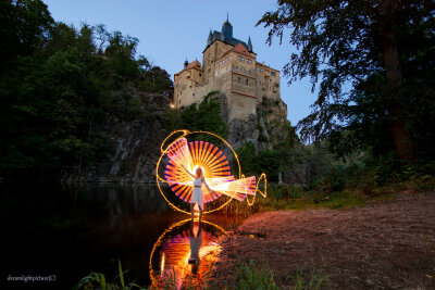Model steht vor der Burg Kriebstein im Wasser. Hinter ihr gelbe und orange Lichtkunst.