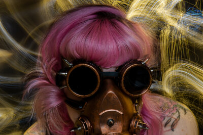 Eine Frau mit pinken Haaren trägt eine mit Farben umspielte Maske.