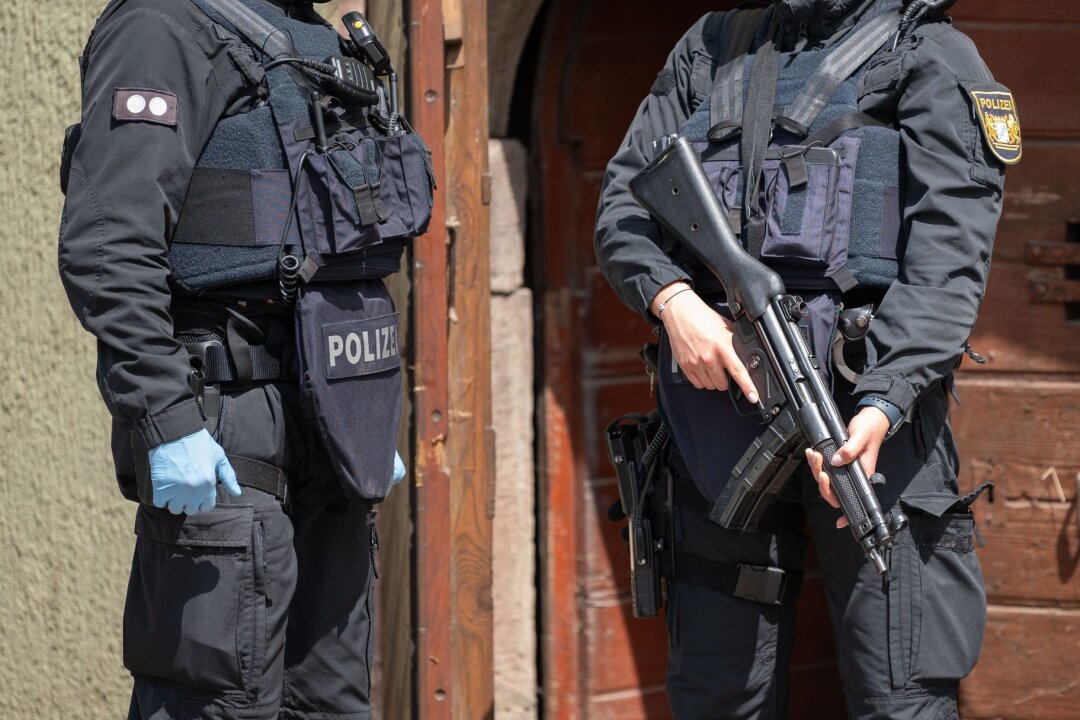 Ermittlungen zu "Reichsbürger"-Razzia im Nordschwarzwald - Eine Polizistin (r) steht mit einer Maschinenpistole vor einer Tür in Althengstett.