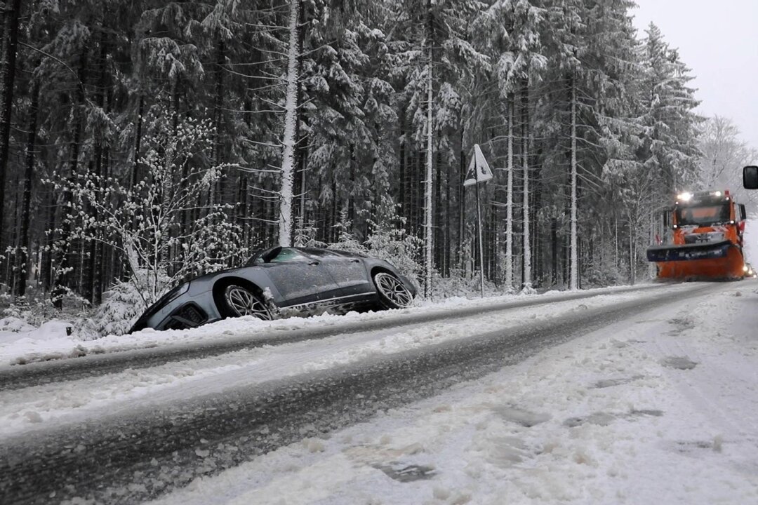 Erzgebirge wieder im weißen Kleid: Kälte bleibt noch - Ein Auto steht nach einem Unfall neben der schneebedeckten Fahrbahn im Graben, während ein Räumfahrzeug angefahren kommt.