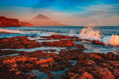 Europäisches Hawaii: Urlaub auf den Azoren - Sonnenuntergang an der Küste von Faial auf den Azoren, mit Blick auf den Vulkan Pico, dem höchsten Gipfel Portugals. 