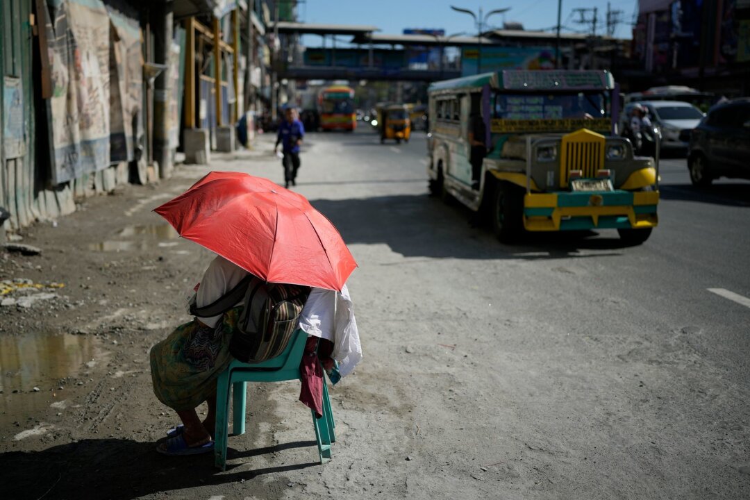 Extremhitze auf den Philippinen - Schulen schließen - Eine Straßenverkäuferin schützt sich in Manila mit einem Regenschirm vor der Sonne.