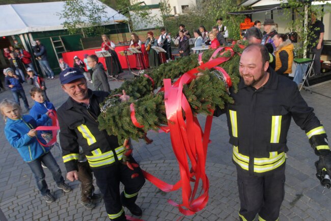 Kameraden stemmen den Maibaum   - Die Kameraden der Freiwilligen Feuerwehr tragen den Maibaum-Kranz auf den Platz. Foto: Thomas Voigt  