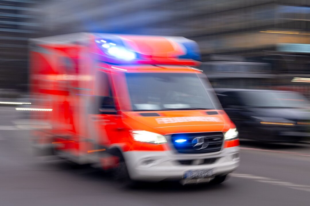 Kollision mit Baum: 46-jähriger Autofahrer schwer verletzt - Ein Rettungswagen der Feuerwehr fährt mit Blaulicht zum Einsatz (Aufnahme mit Langzeitbelichtung).