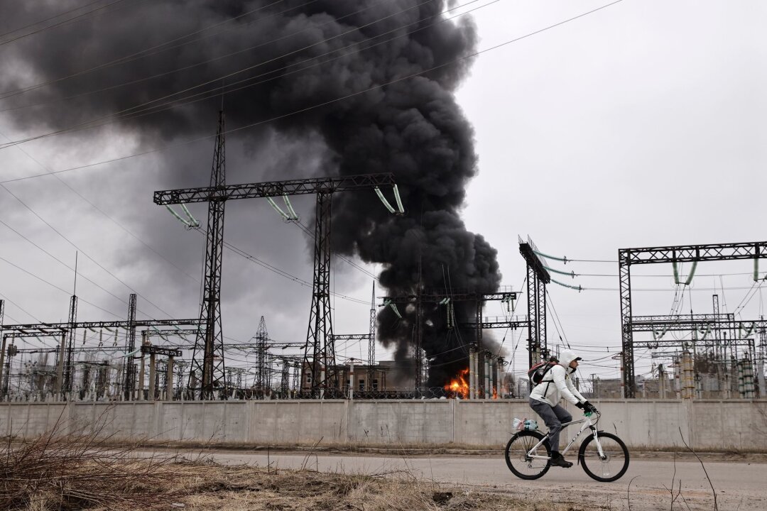 Krieg gegen die Ukraine: So ist die Lage - Nach einem russischen Angriff fährt ein Mann mit seinem Rad an einem brennenden Elektrizitätswerk in Charkiw vorbei.