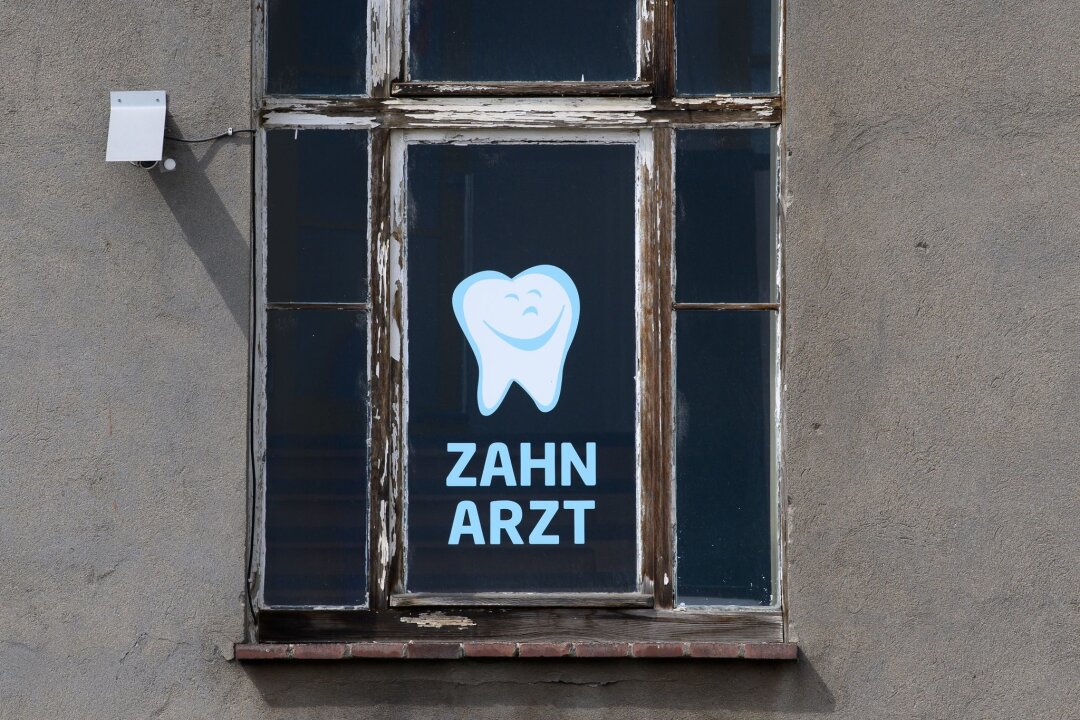 Landeszahnärztekammer fördert Berufseinstige - Zahnarzt steht an einem Fenster eines Hauses, in dem sich eine Zahnarztpraxis befindet, geschrieben.