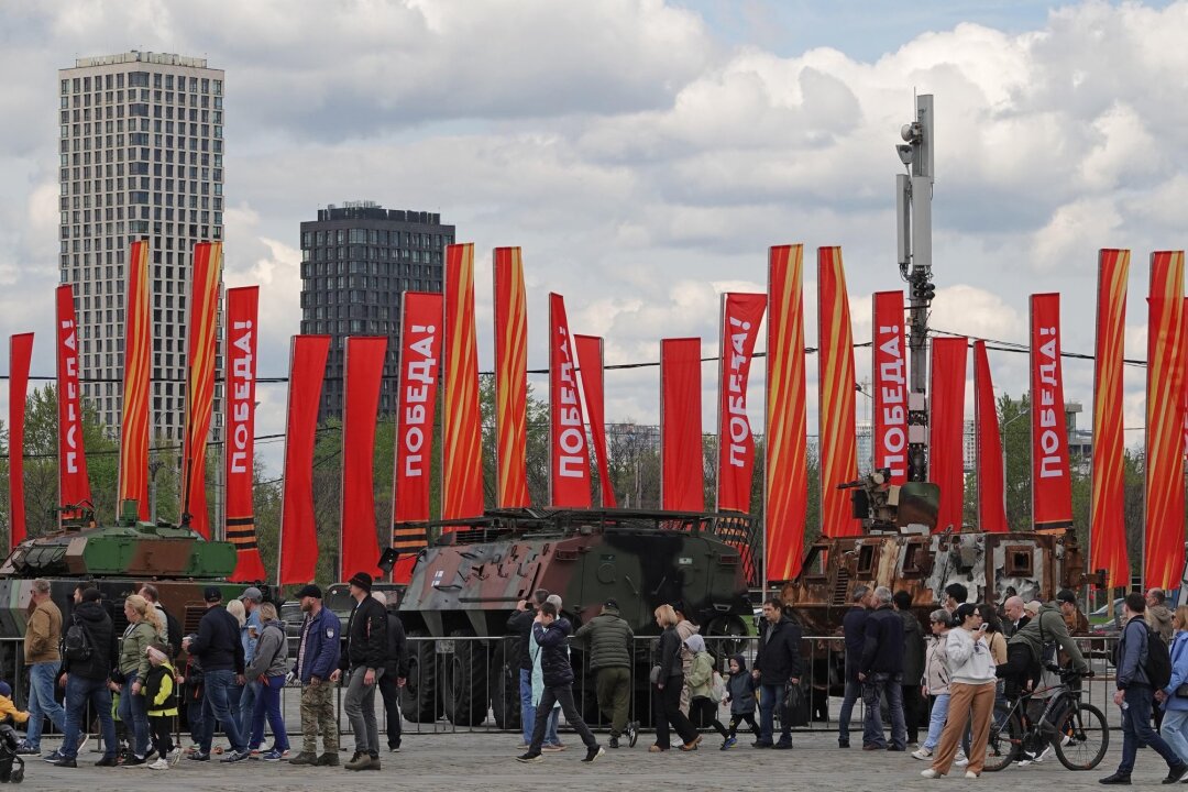 Parade ohne Sieg - Putin rüstet sich für langen Krieg - Menschen besichtigen eine Schau zu Kriegstrophäen im Park Pobedy (Park des Sieges) in Moskau. Gezeigt wird Militärtechnik aus verschiedenen westlichen Ländern und der Ukraine. Im Hintergrund zu sehen sind rote Fahnen mit der Aufschrift Pobeda! (auf Deutsch: Sieg).