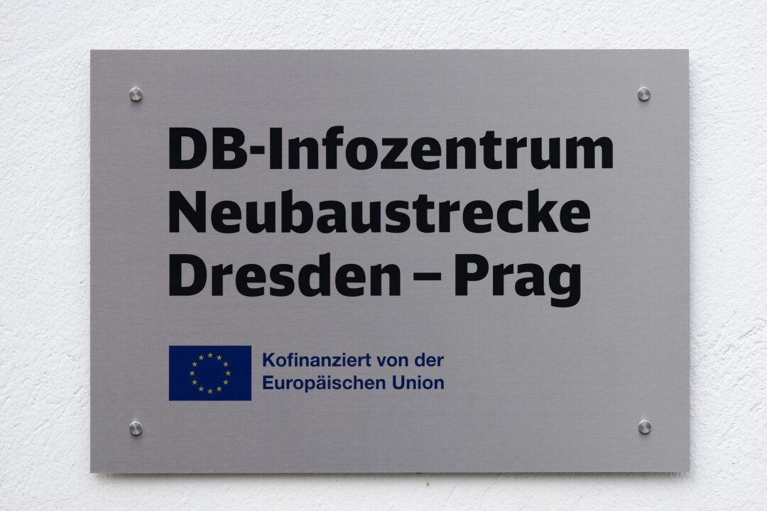 Planung für Eisenbahntunnel im Erzgebirge fast abgeschlossen - Ein Schild mit der Aufschrift „DB-Infozentrum Neubaustrecke Dresden - Prag“ hängt an einem Gebäude.