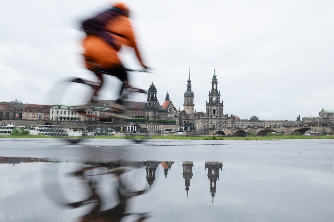 Regen und Gewitter in Sachsen - am Samstag mögliche Unwetter - Ein Radfahrer fährt am Ufer entlang. Die Kulisse der Altstadt spiegelt sich in einer Pfütze am Ufer der Elbe.