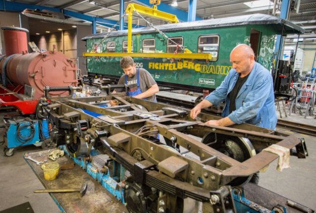 Uwe Gülzow und Uwe Mehnert (v.l.) arbeiten an einem der Drehgestelle für den Wagen der Fichtelbergbahn. Foto: Jan Görner