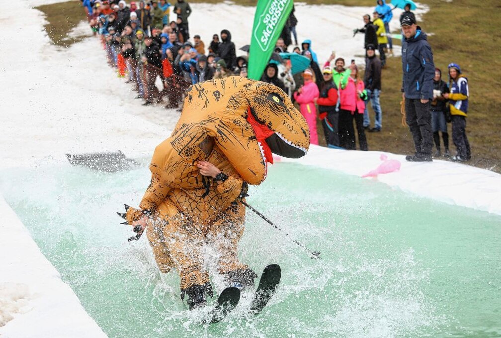 Skiparty läutet am Fichtelberg Wintersport-Saison aus - Auch ein Dinosaurier (Ruben Kretzschmar) wagte sich übers eiskalte Wasser zu schlittern. Foto: Thomas Fritzsch