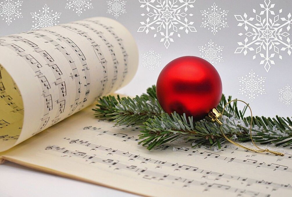 Weihnachtsliedersingen im Tietz - Ein Notenblatt und eine rote Weihnachtskugel liegen auf einem weißen Tisch. Foto: Symbolbild/Pixabay
