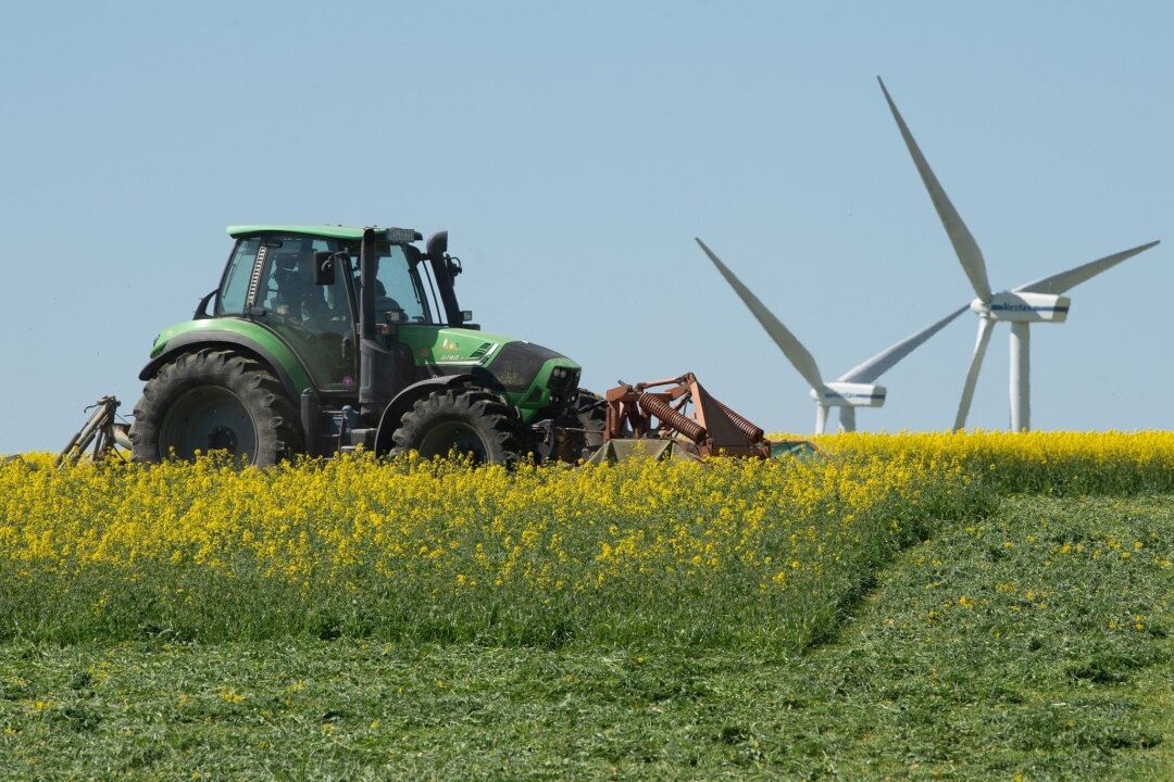 Zahl der Ökobetriebe in der Landwirtschaft gestiegen - Ein Landwirt fährt vor einer Windkraftanlage mit einem Traktor über ein Rapsfeld.